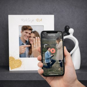 Bijeli drveni okvir za zaruke s rukom ispisanim imenima zaručnika i datumom, ukrašen motivima prstenja i srca.